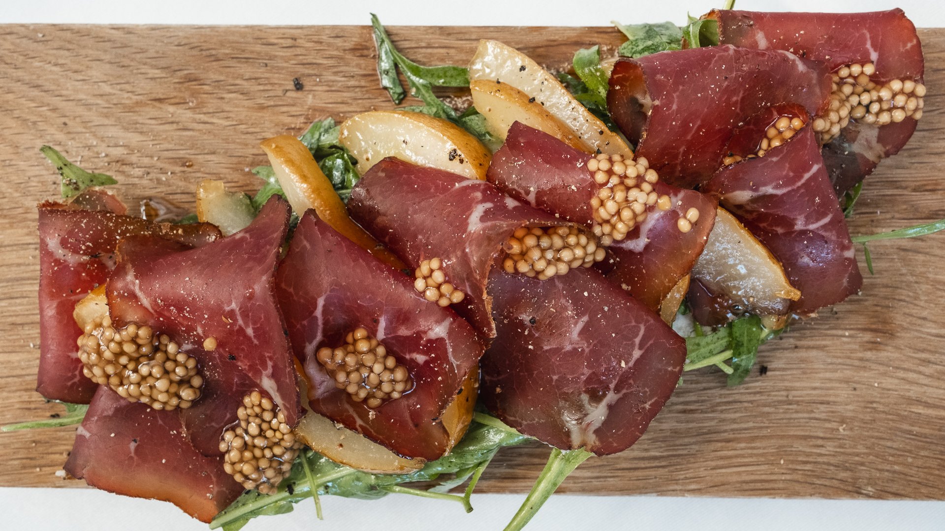 Inn & Restaurant in Parsberg serving regional cuisine Slices of meat with mustard seeds, pear wedges and greens on a wooden board
