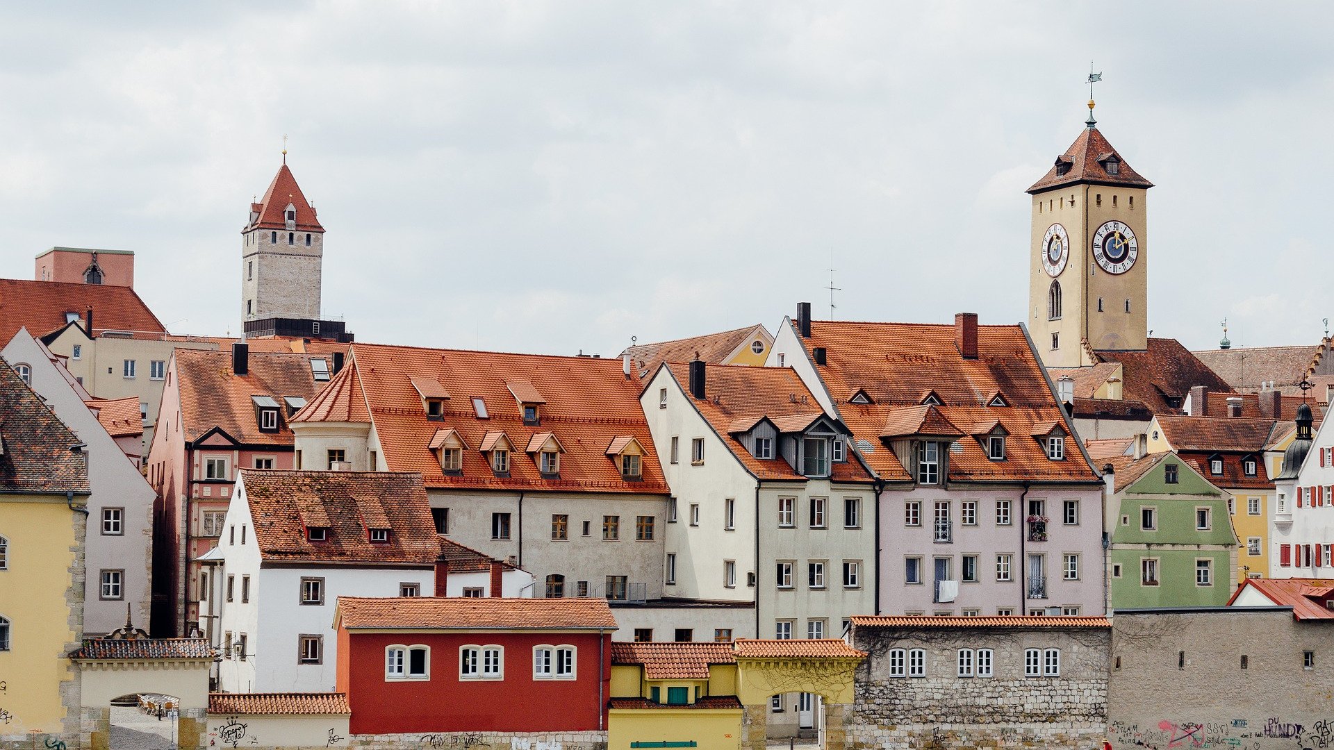 Hotels in Regensburg and its surroundings: culturally rich! Historic houses and clock tower by riverbank under cloudy sky