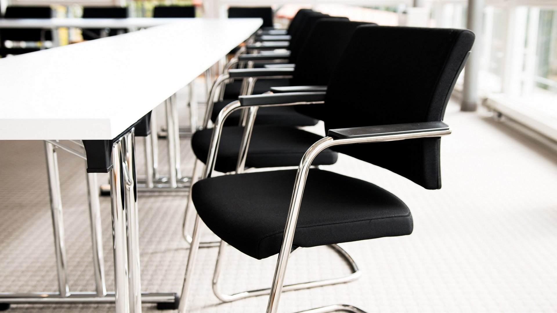Services and rates for conferences and celebrations Empty black chairs along a white conference table in a bright room