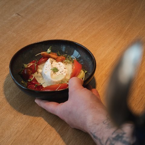 Restaurant in Parsberg: Enjoy gourmet Hand holding bowl with burrata cheese and tomatoes on wooden table