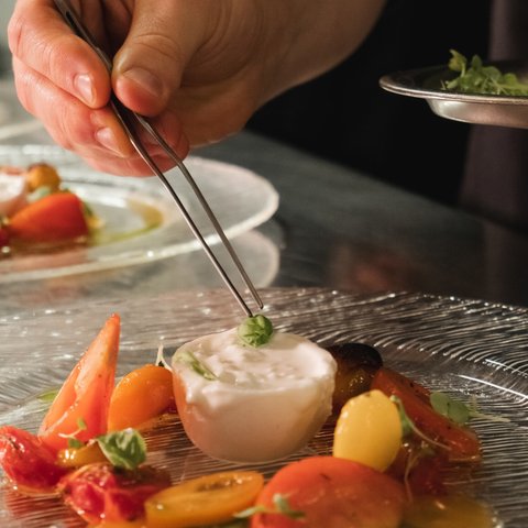 Restaurant in Parsberg: Enjoy gourmet Hand placing basil leaf on burrata cheese with tomatoes on plate