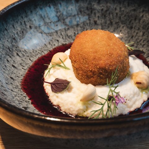 Restaurant in Parsberg: Enjoy gourmet Breaded fried ball on creamy puree with nuts and herbs in black bowl