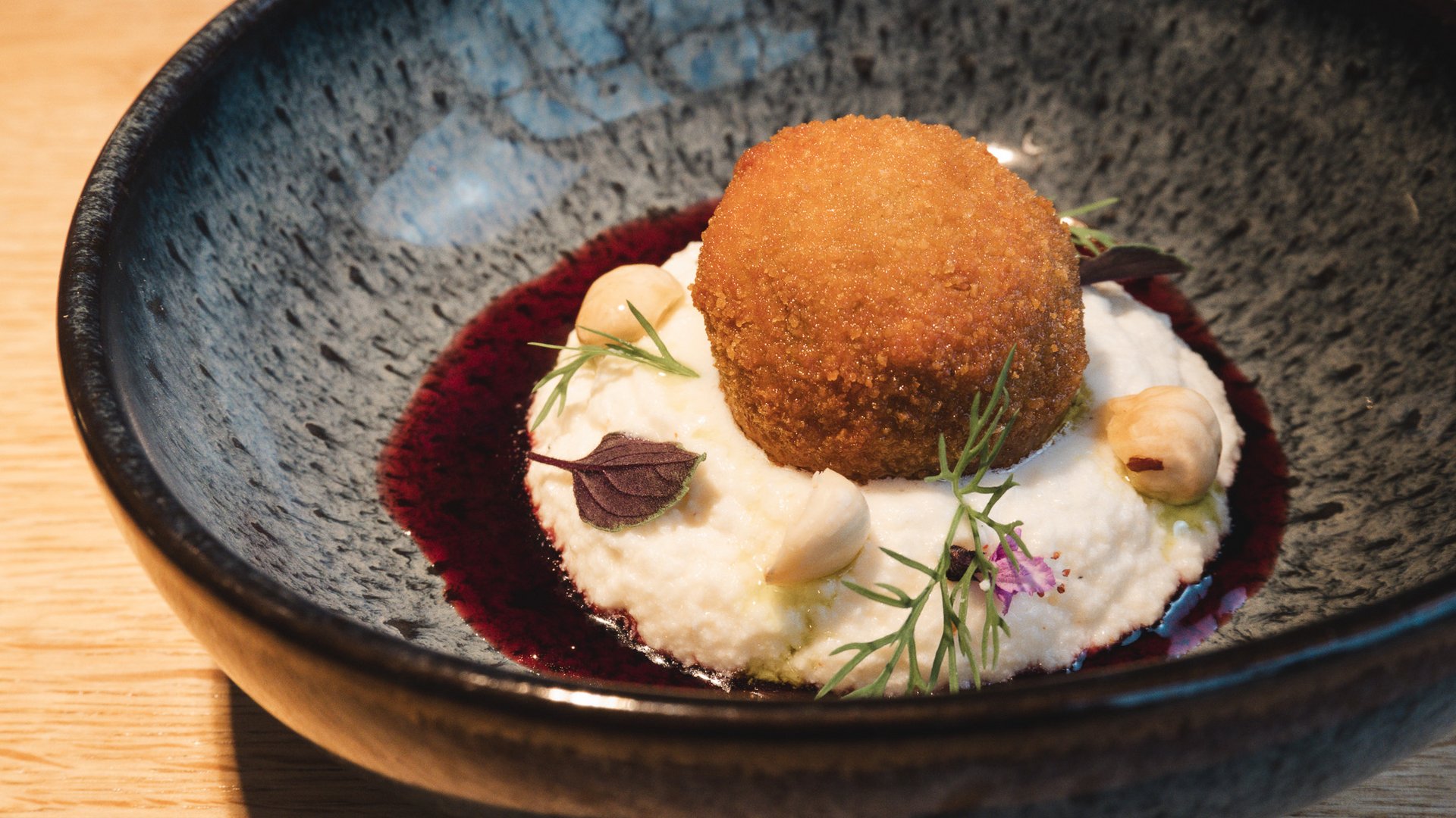 Restaurant in Parsberg: Enjoy gourmet Breaded fried ball on creamy puree with nuts and herbs in black bowl