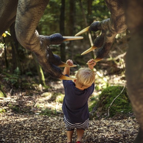 Hotels in Regensburg and its surroundings: culturally rich! Child touching claws of a dinosaur figure in the forest while a photographer takes photos