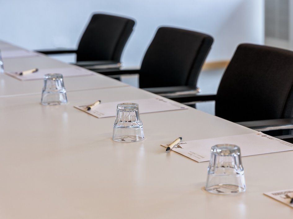Services and rates for conferences and celebrations Conference table with chairs, glasses, notepads, and pens arranged