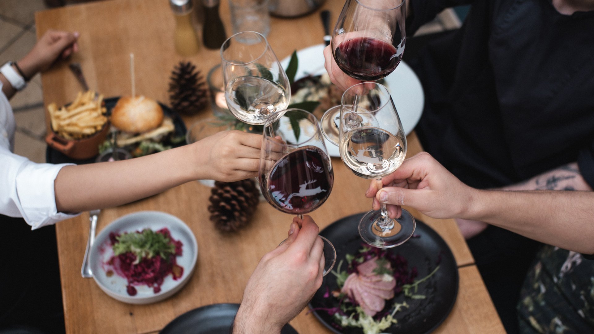 Home Menschen stoßen mit Rot- und Weißweingläsern über einem gedeckten Tisch an