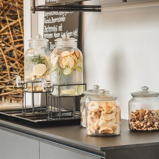 Home Wasserspender mit Früchten und Gläser mit Nüssen und getrocknetem Obst auf schwarzer Theke