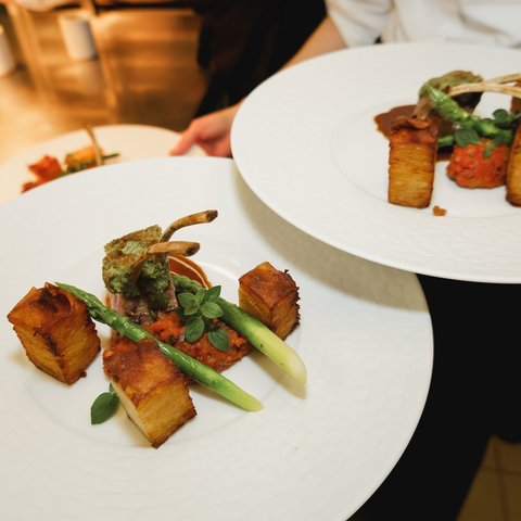 Restaurant in Parsberg: Enjoy gourmet Plated lamb chops with potatoes, asparagus, and tomato sauce on white plates.