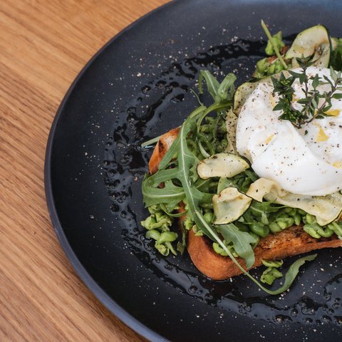 Gasthof & Restaurant in Parsberg mit regionaler Küche Toast mit Avocado, Rucola, Zucchinichips und pochiertem Ei auf schwarzem Teller