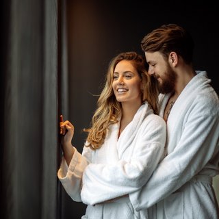 Beer garden love Couple in white bathrobes smiling and looking out the window
