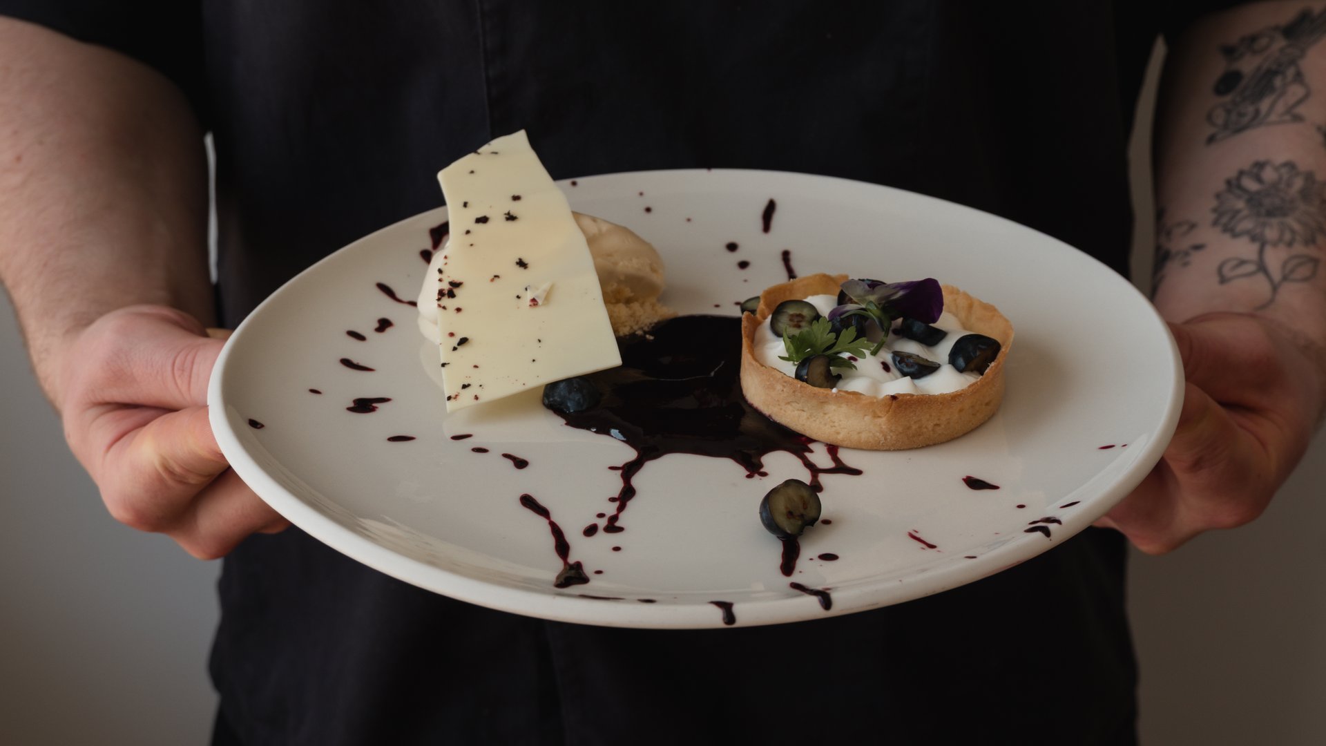 Restaurant in Parsberg: Enjoy gourmet Hand holding plate with dessert tart, berries, white chocolate, and sauce