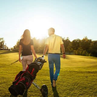 Hotels in Regensburg and its surroundings: culturally rich! Couple walking on golf course with golf bag in sunny weather