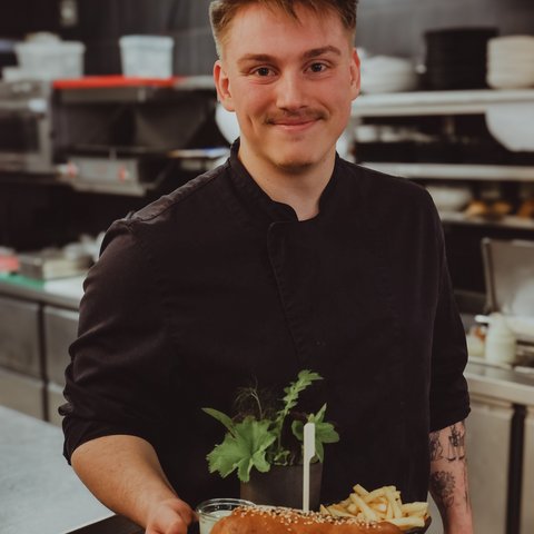 Gasthof & Restaurant in Parsberg mit regionaler Küche Koch hält Teller mit Sandwich, Pommes und Kräutern in einer Restaurantküche