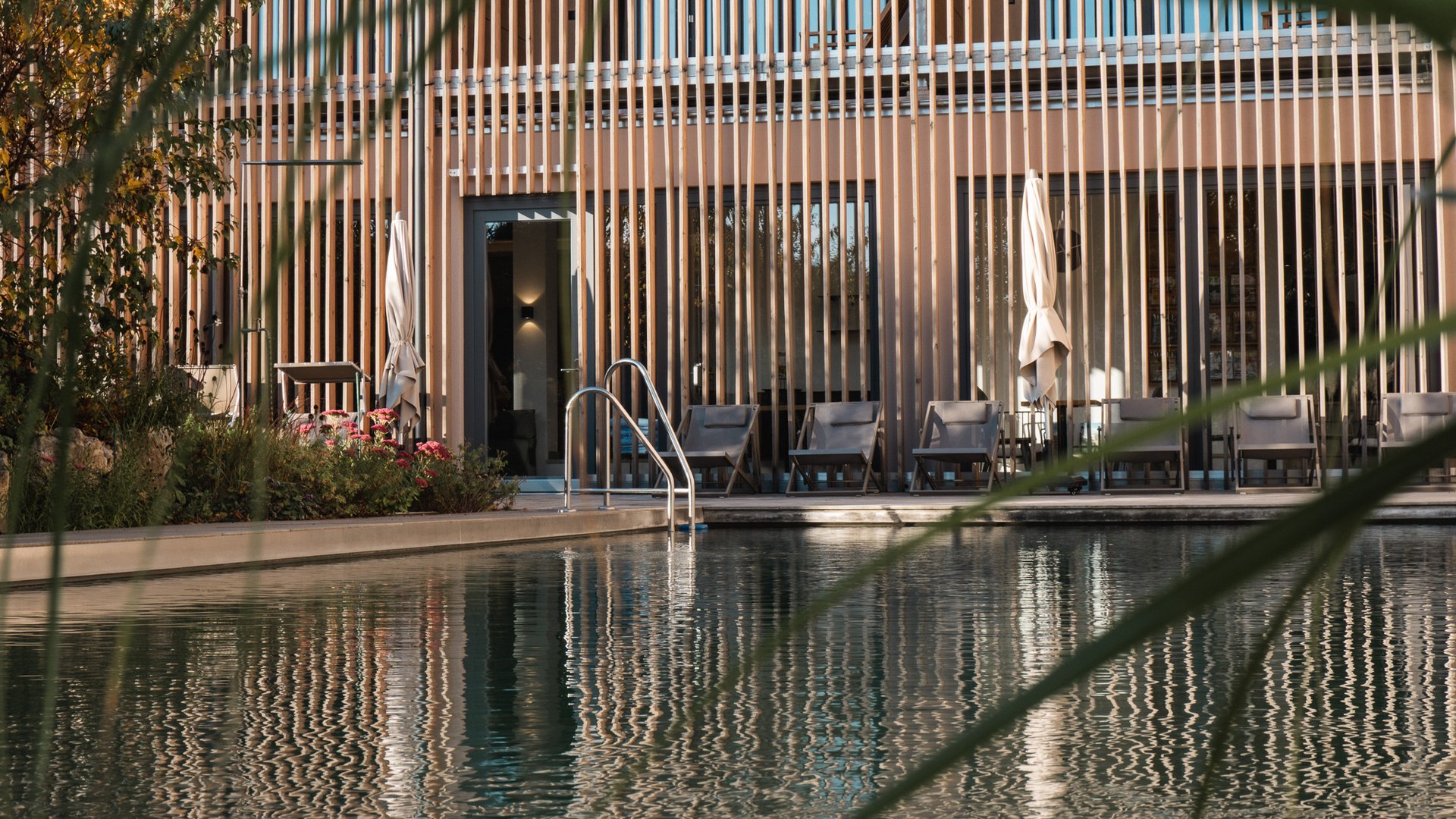 Wellnesshotel Parsberg – Romantik Hotel Hirschen Außenpool mit Liegestühlen vor einem modernen Gebäude mit vertikaler Holzverkleidung