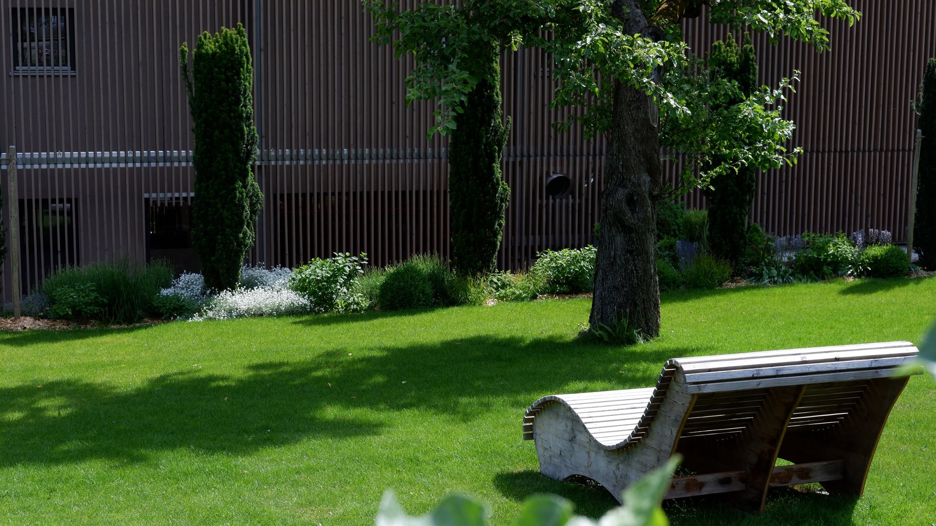 Services and rates for conferences and celebrations Green lawn with modern wooden lounge chair and trees in the background