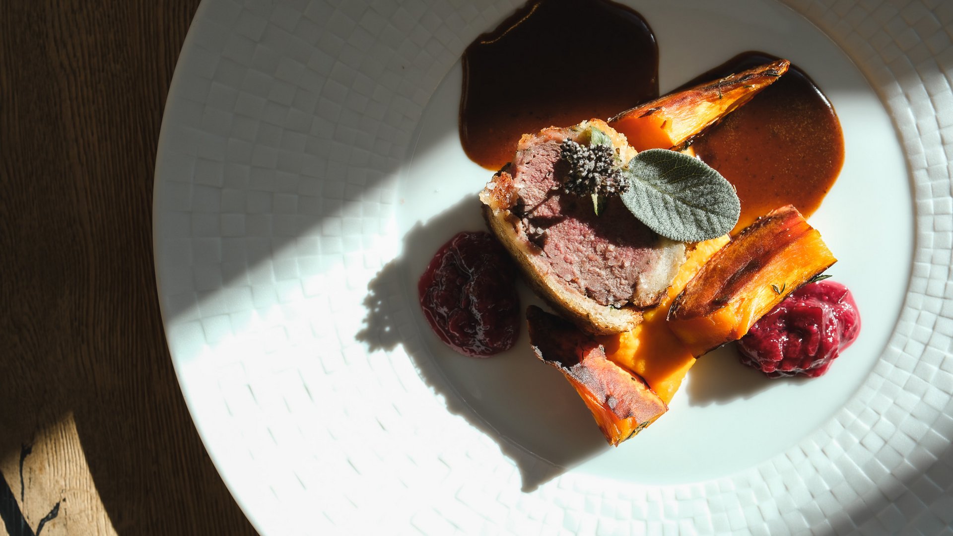 Wellnesshotel Parsberg – Romantik Hotel Hirschen Aufgeschnittenes Fleisch mit geröstetem Gemüse, Sauce und Salbei auf einem weißen Teller