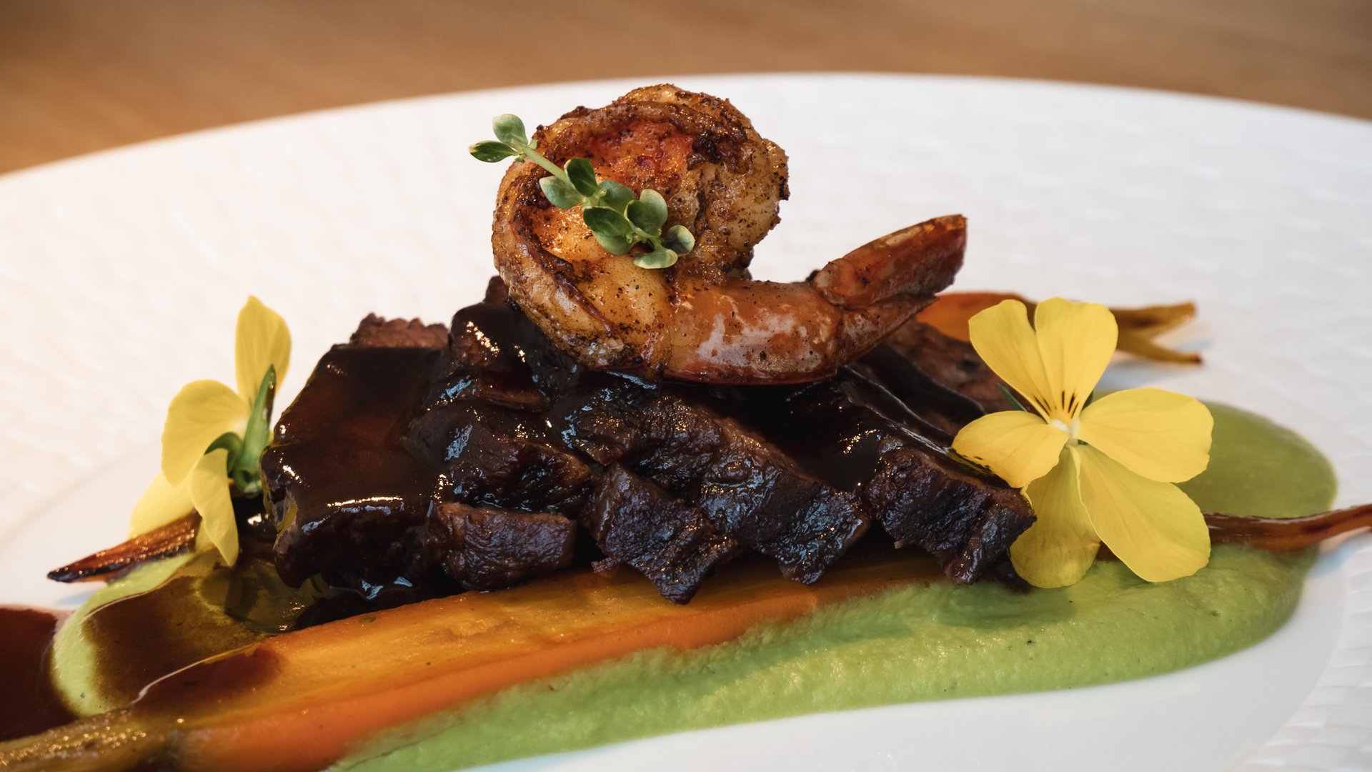 Home Gourmetgericht mit gebratener Garnele, Fleisch, Karotte und Blumen auf grünem Püree