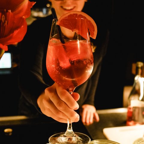 Gasthof & Restaurant in Parsberg mit regionaler Küche Person reicht ein Glas mit rotem Cocktail und Grapefruitzeste an einer Bar