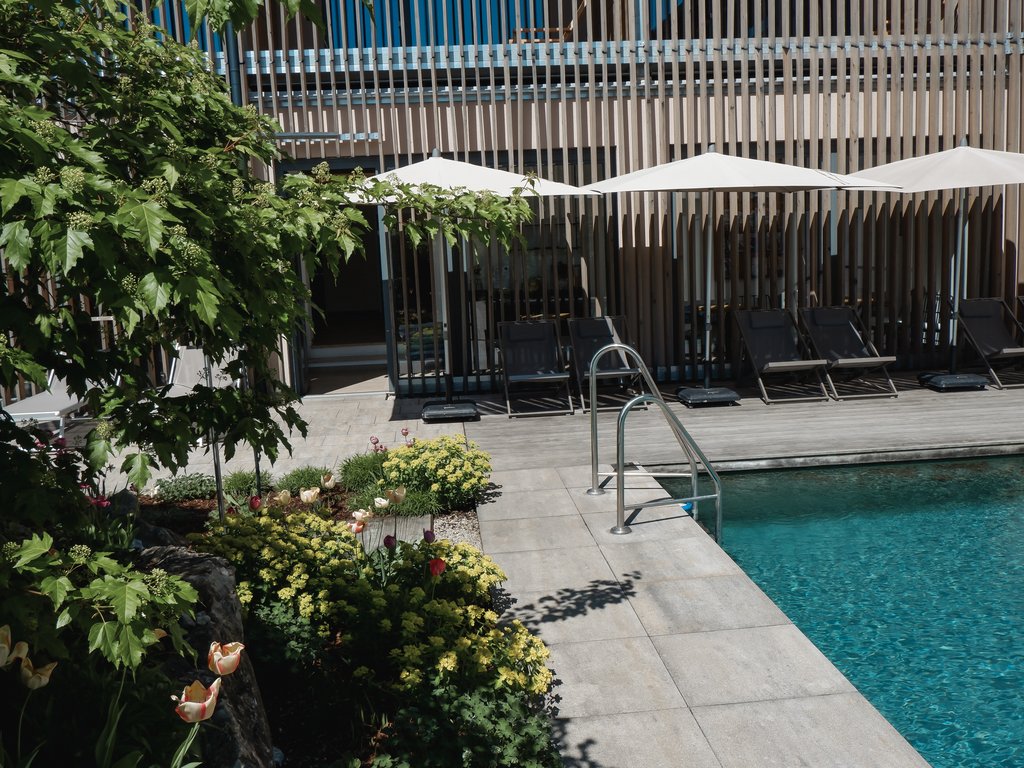 Wellnesshotel Parsberg – Romantik Hotel Hirschen Pool mit Liegestühlen und weißen Sonnenschirmen neben einem Blumenbeet
