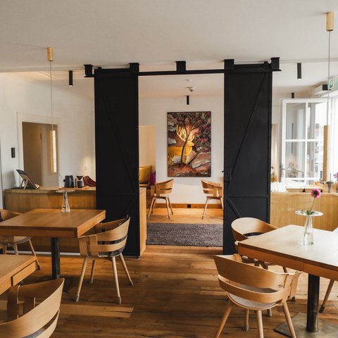 Restaurant in Parsberg: Enjoy gourmet Cozy restaurant with wooden tables and chairs, flower decor, and wall art