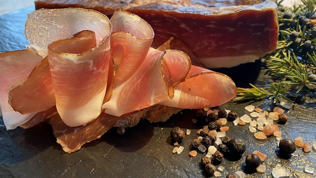 Gasthof & Restaurant in Parsberg mit regionaler Küche Aufgeschnittene luftgetrocknete Speckscheiben mit Gewürzen und Kräutern auf schwarzem Stein