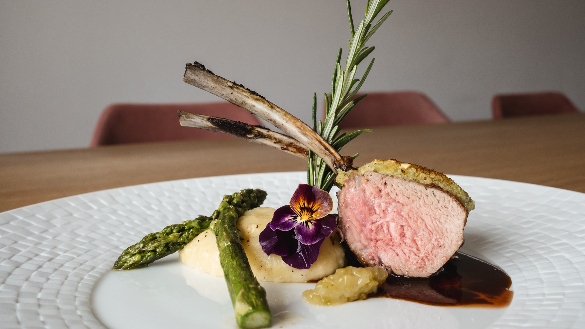 Home Lammkotelett mit Kräuterkruste, Spargel und Blumendekoration auf weißem Teller