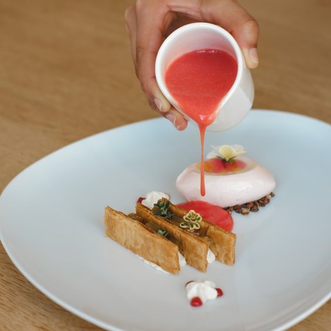 Restaurant in Parsberg: Enjoy gourmet Hand pouring red sauce on fine dessert on white plate